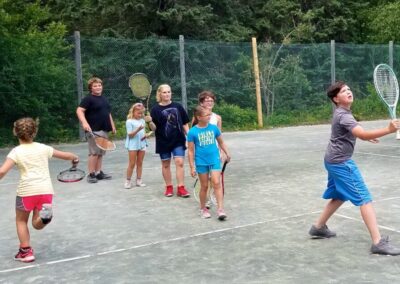 Color photo of EdGE students practicing tennis during a learning clinic. They wear shorts and t-shirts while swinging tennis rackets.