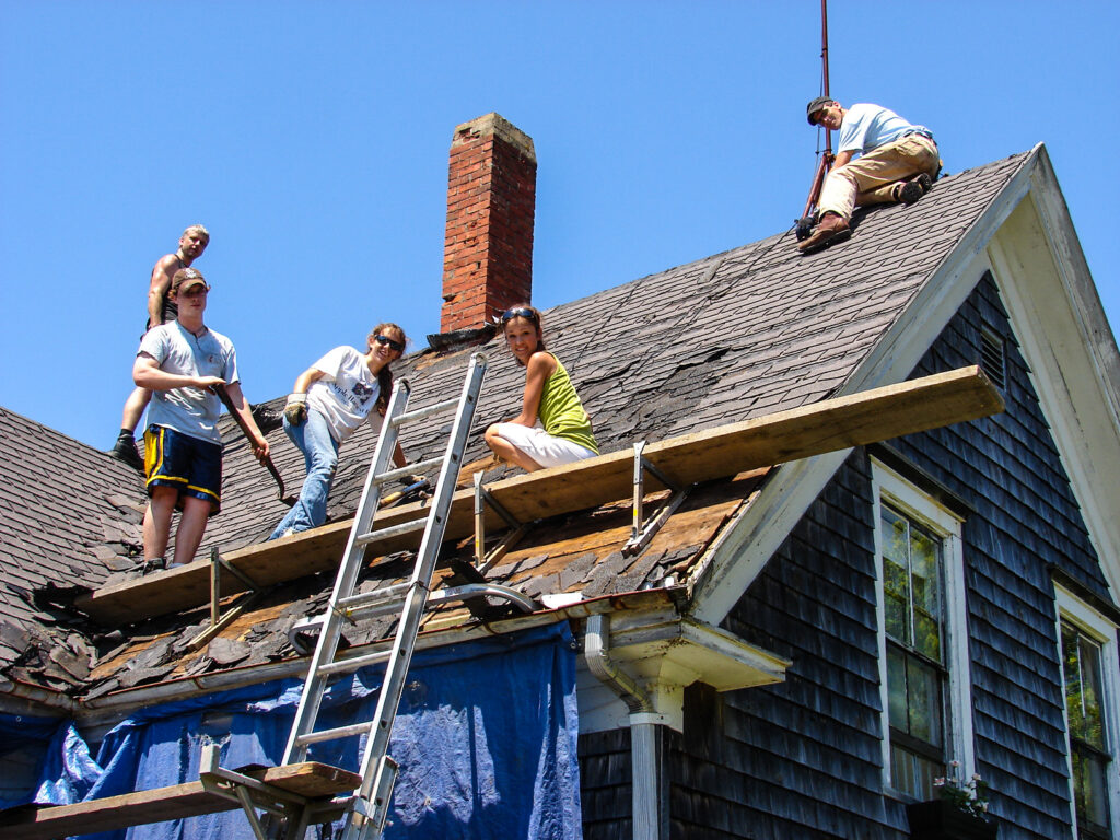 Color photo of Housing Rehab program volunteers scraping off roof shingles