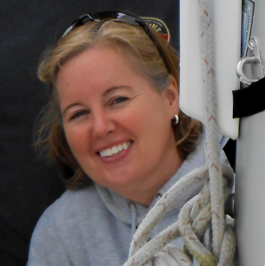 Color photo of Erica Hutchinson smiling. She has white skin, and a gray-blonde bob and wears a black jacket.