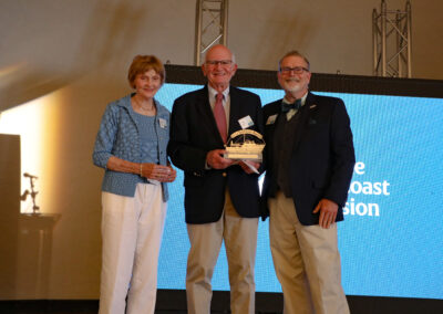 Color photo of EdGE founder Connie Greaves Bates, Sunbeam awardee Les Coleman, and President John Zavodny stand on-stage and smile.