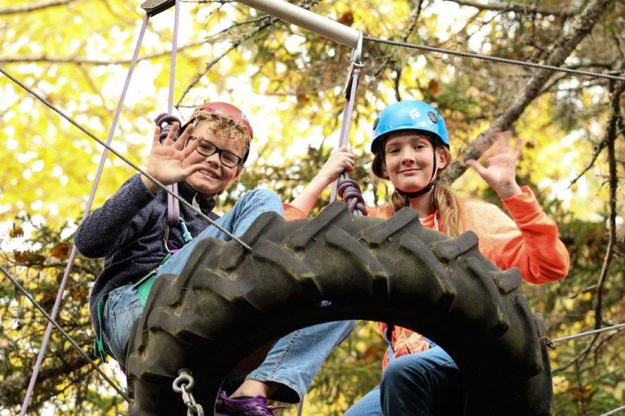 Color of photo of two white children wearing helmets on the high ropes course