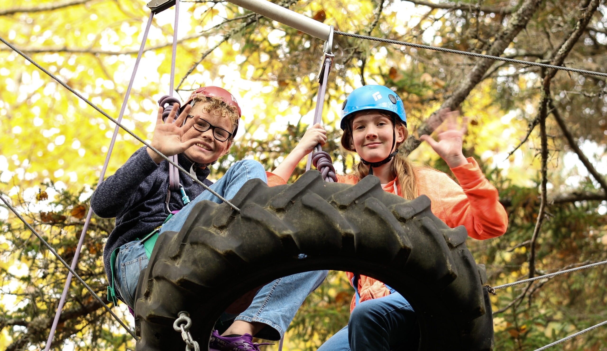 Color of photo of two white children wearing helmets on the high ropes course