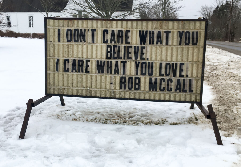 A color photo of a sign that says "I don't care what you believe. I care what you love - Rob McCall"