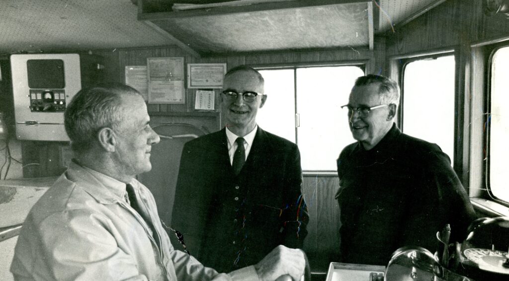 A black and white photo of three men standing in the pilot house of a boat