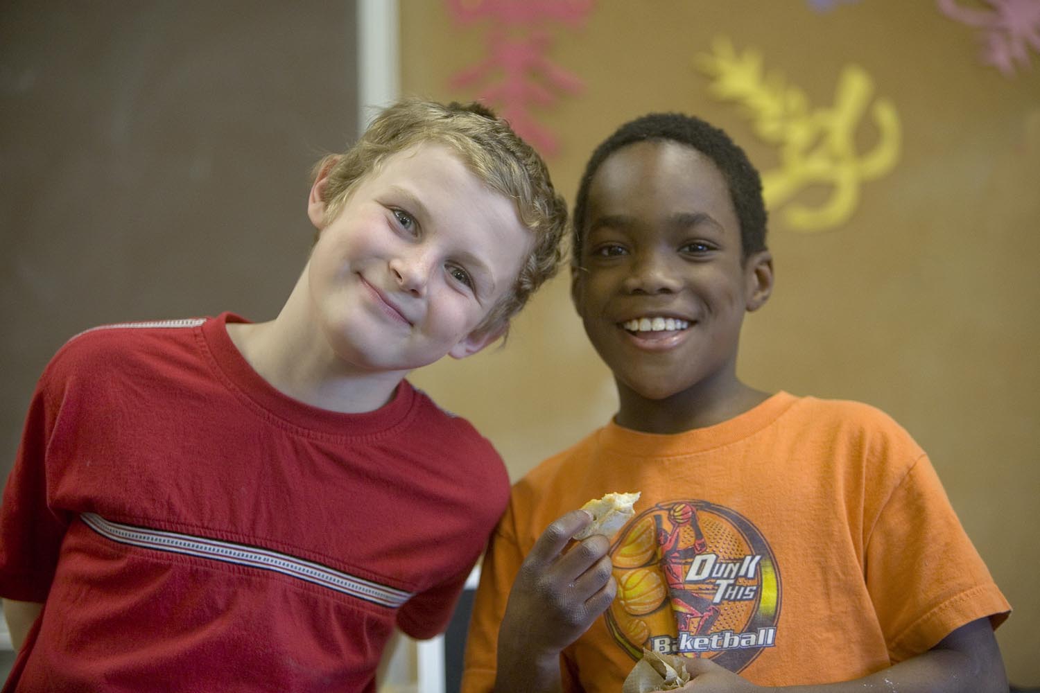 A color photo of two children, one white male, one black male, smiling at the camera