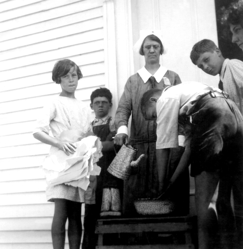 A black and white photo of five students and a nurse. The students are washing their hands in a basin.