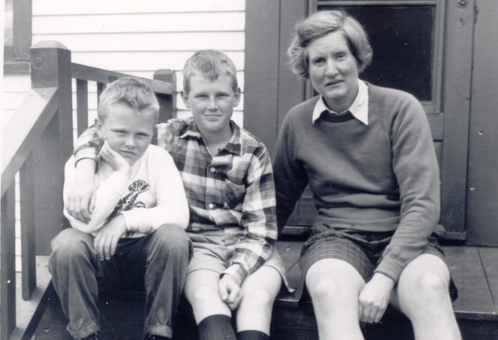 A black and white photo of two boys and and older woman sitting on the front steps of a house