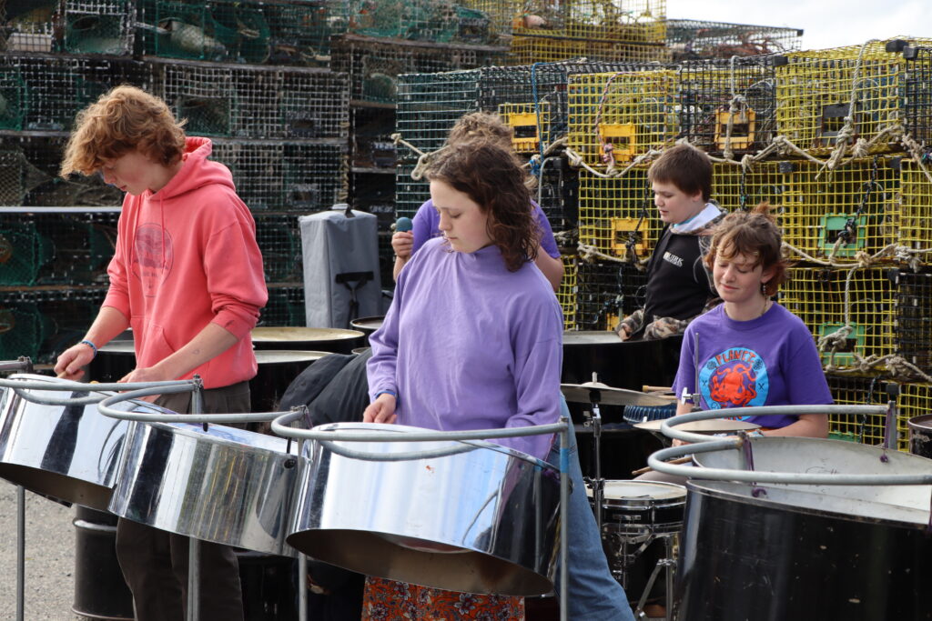 Four students play steel pan in front of lobster traps
