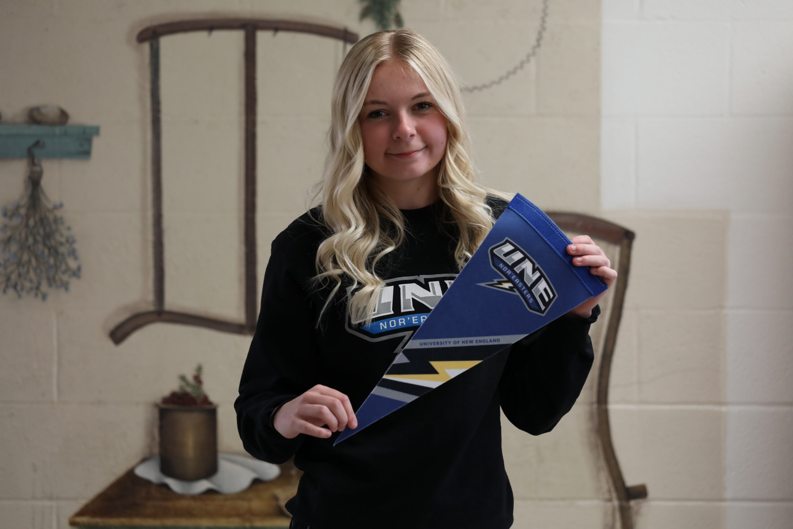 A photo of a young smiling white woman holding a college pennant that says UNE