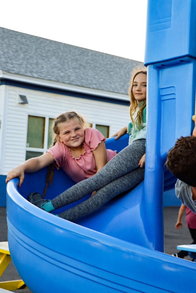 Two young girls smile while sitting on a slide
