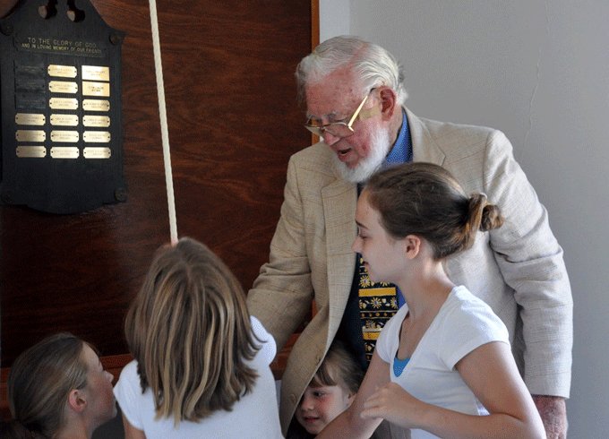 An older white gentleman chats with young children.