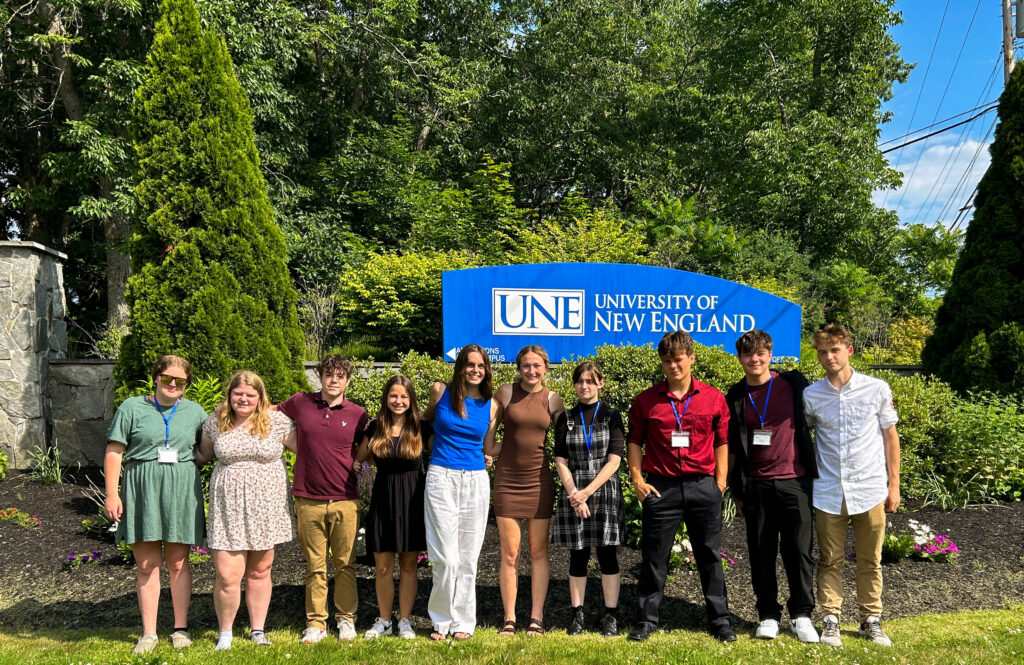 A group of students standing in front of a sign that says University of New England