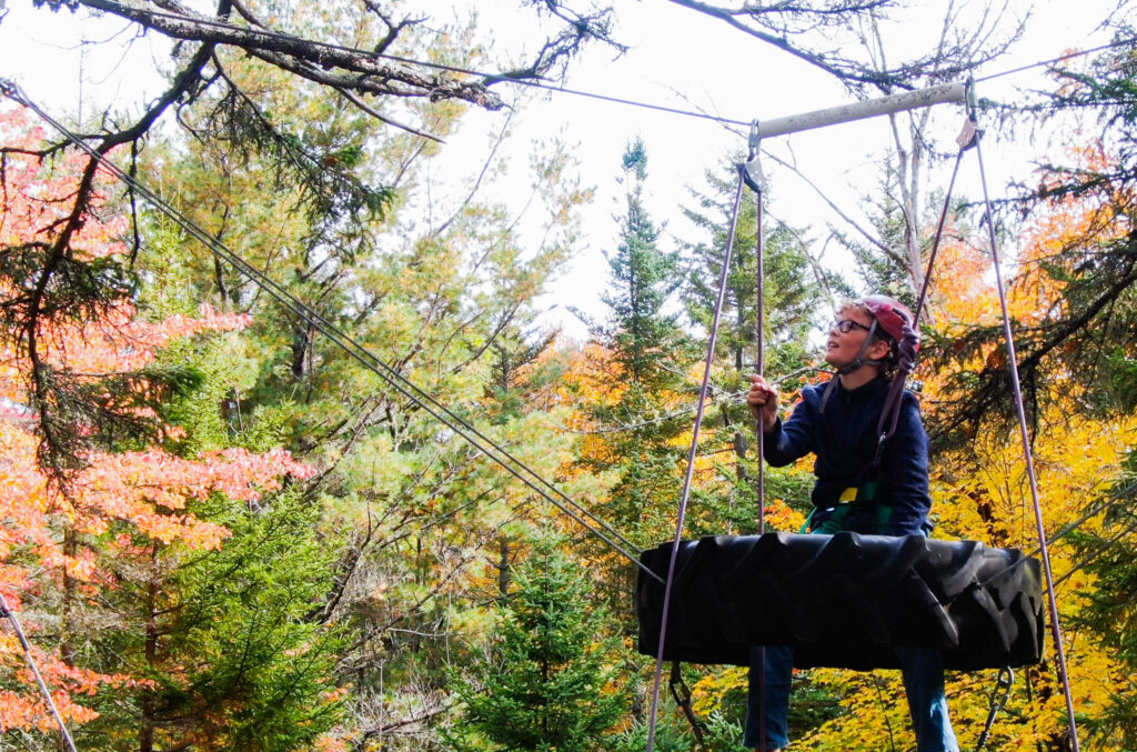A color photo of a student sitting on the ropes course during fall