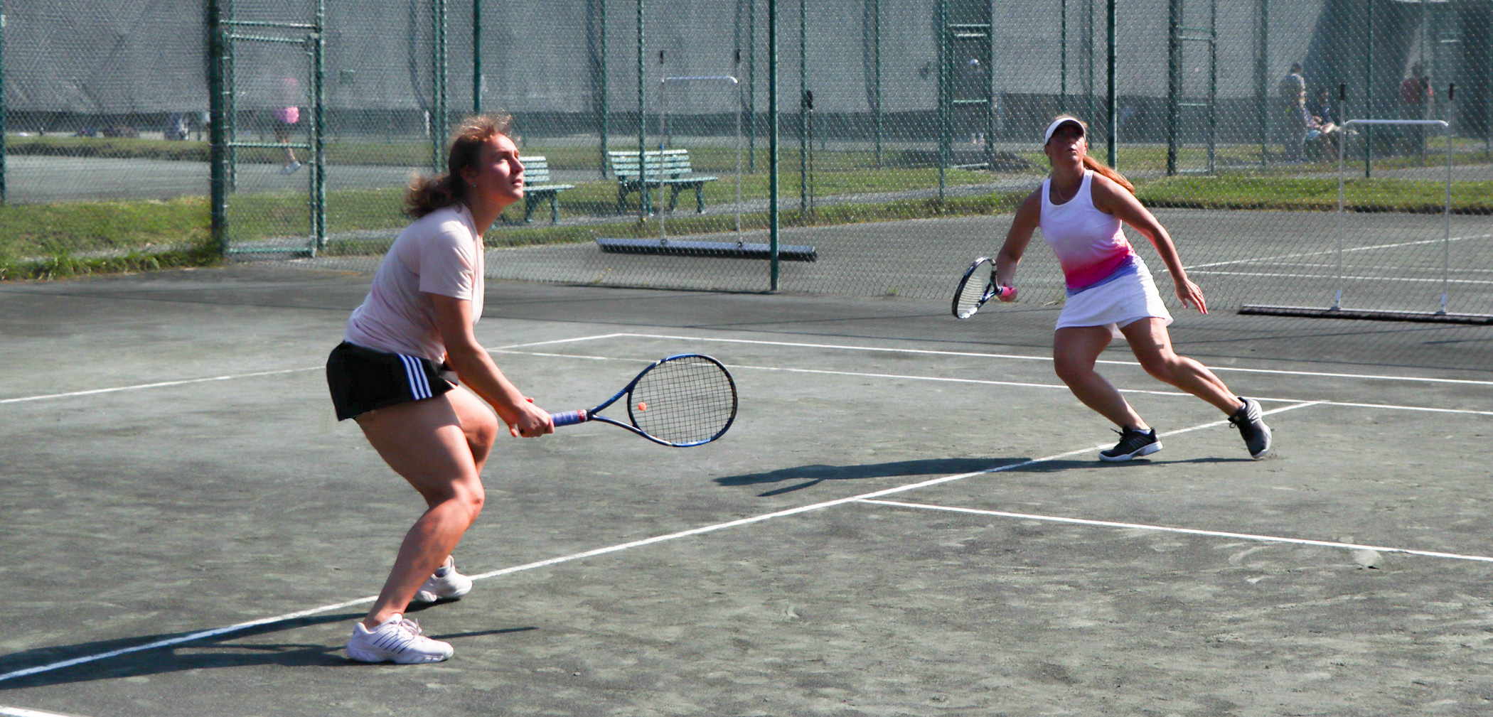 Two white women take an athletic stance on a tennis court.