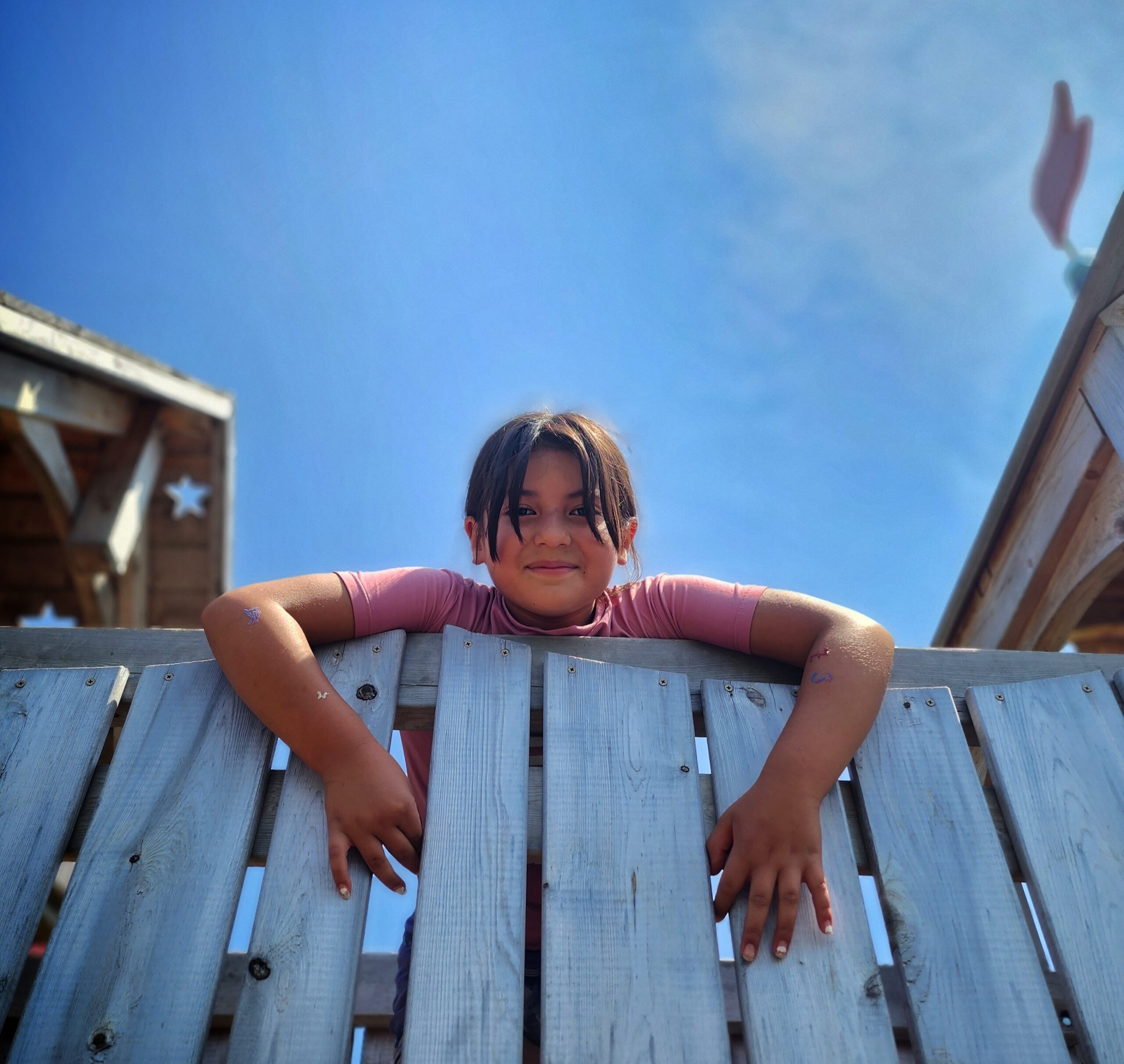 A young girl looks down on a play structure. She is smiling. 