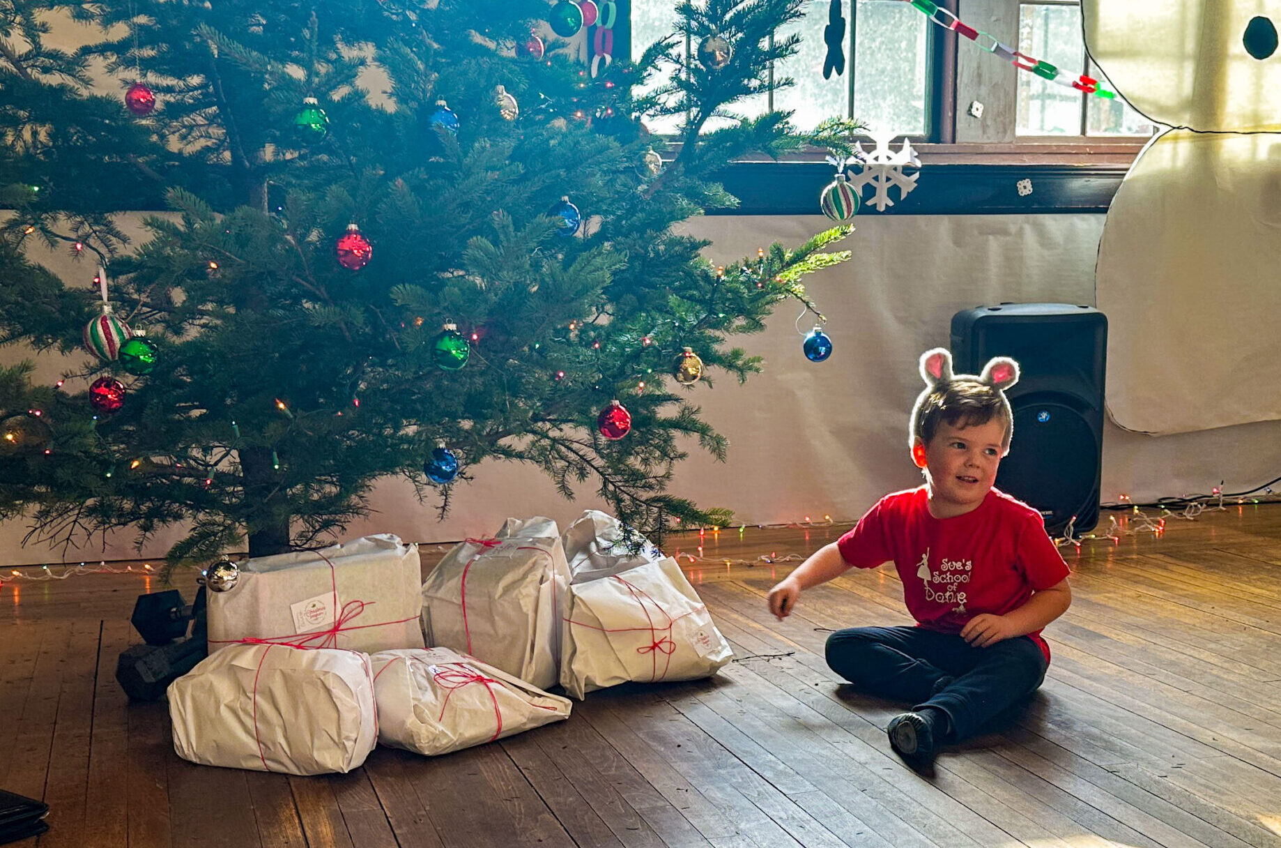 A small boy sits in front of a Christmas tree with presents underneath it. 
