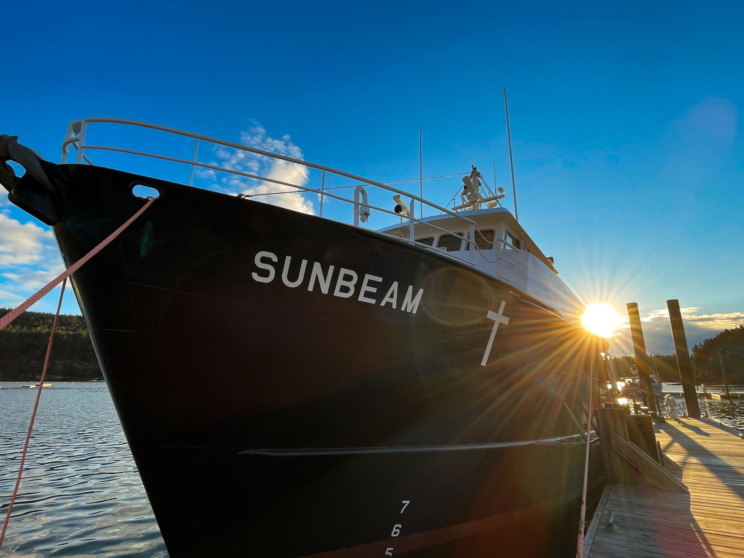 A photo of the Sunbeam boat taken with the name on the hull. The sun is peaking out behind the boat. 