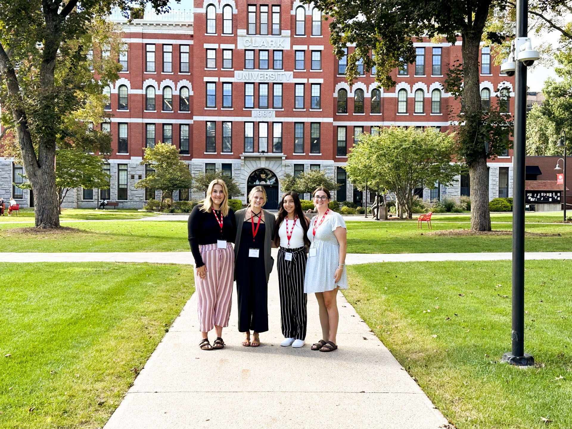 Four young women stand in front of a building that reads "Clark University" 