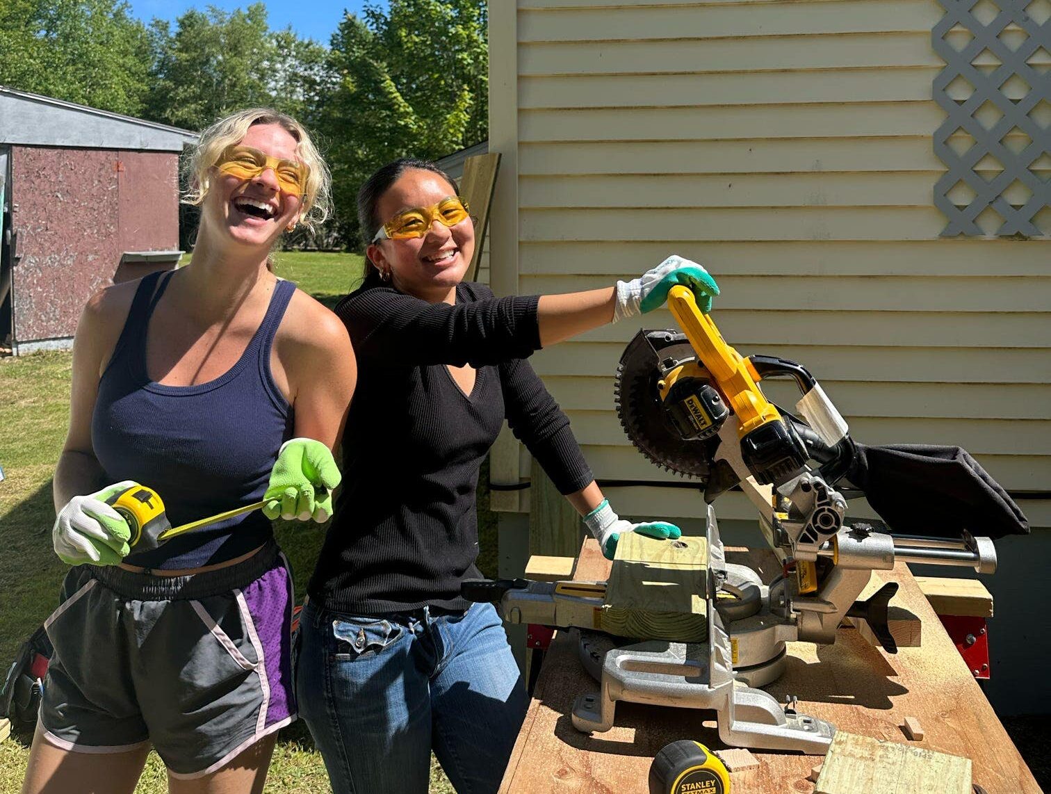 Two college student women with tools in front of a house