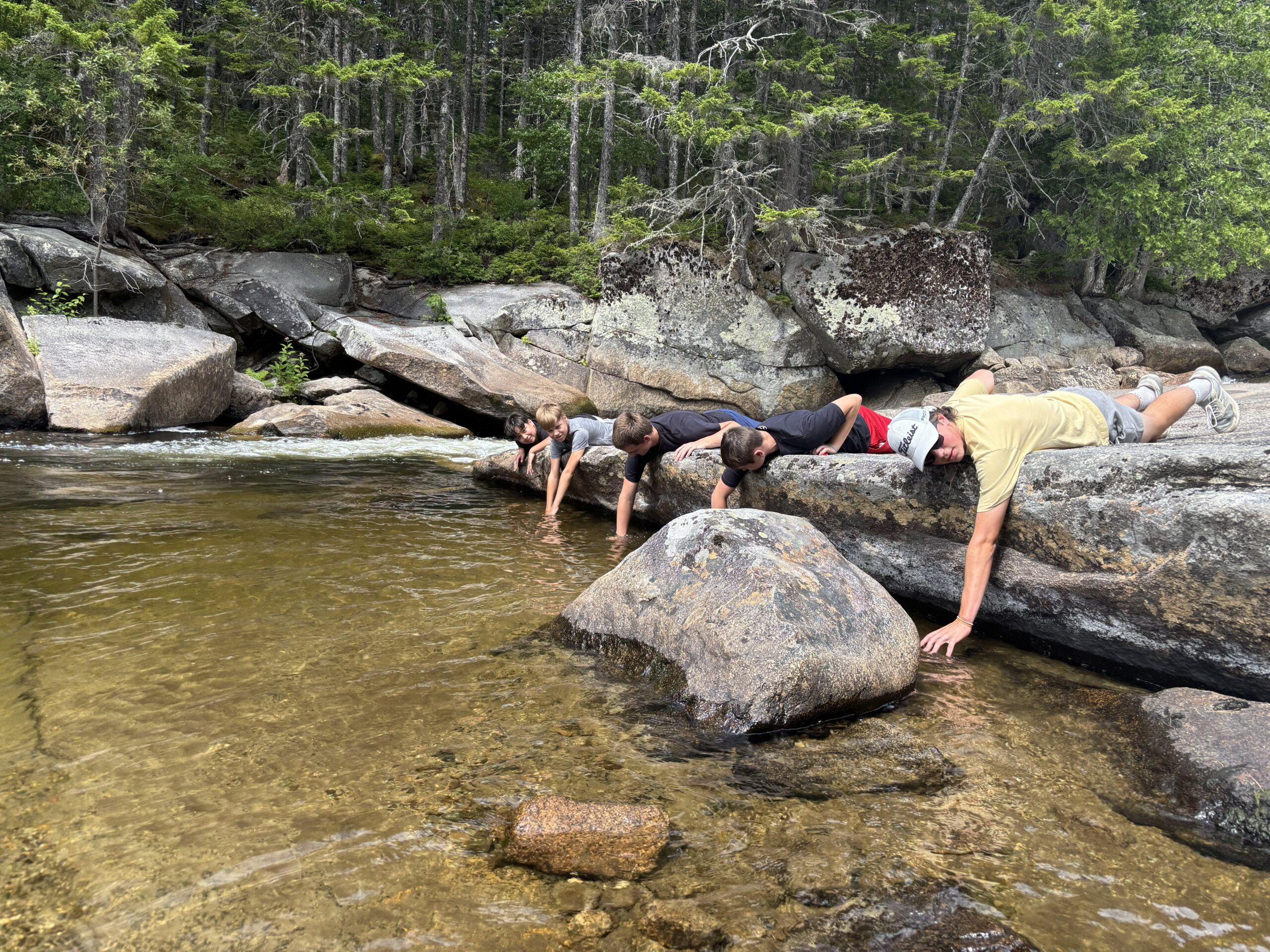 Journey boys laying on rock in front of river 